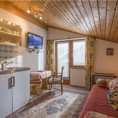 Ein gemütliches Wohnambiente mit Holzdecke, einer kleinen Küche und einem Fernseher. Ein Sofa und ein Tisch schaffen eine einladende Atmosphäre.