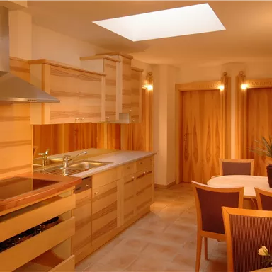Eine moderne Küche mit Holzschränken und einem großen Fenster. Ein Esstisch mit Stühlen lädt zum Verweilen ein.