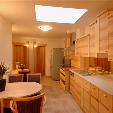 Eine moderne Küche mit hellen Holzschränken und einem Essbereich. Ein Oberlicht sorgt für viel Tageslicht im Raum.
