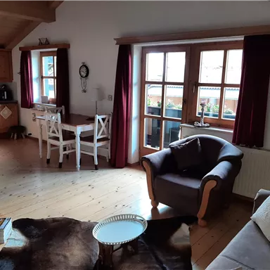 A cozy living room with an armchair and a table. Large windows provide plenty of daylight and an inviting atmosphere.