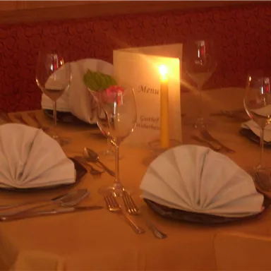 An elegantly set table with folded napkins and glasses. A candle and a menu card are also present.
