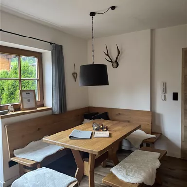 A cozy dining area with a wooden table and chairs. Decorative elements hang on the wall, and a window lets in a lot of light.