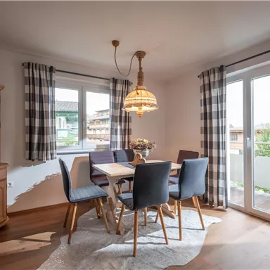 A cozy dining area with a wooden table and chairs. Large windows provide plenty of daylight and a view outside.