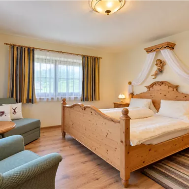 Ein gemütliches Schlafzimmer mit einem Holzbett und einer komfortablen Sitzecke. Helle Farben und natürliche Materialien schaffen eine einladende Atmosphäre.
