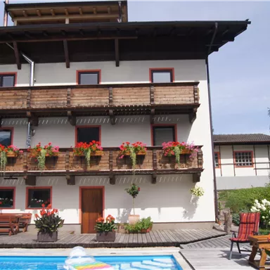 Ein hübsches Haus mit Balkonen und blühenden Pflanzen. Der Swimmingpool im Vordergrund lädt zum Entspannen ein.