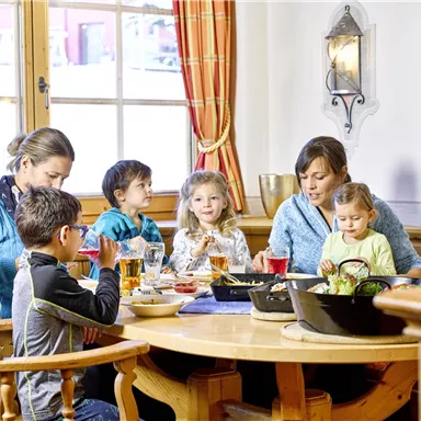A cheerful group of adults and children is sitting around a table, enjoying a meal together. The ambiance is cozy and inviting.
