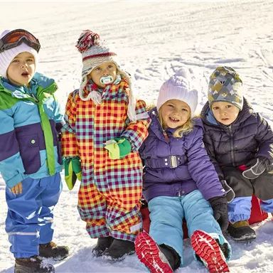Four joyful children are playing in the snow, dressed in colorful winter clothing. They are sitting on sleds and enjoying the sunny day.