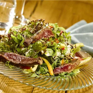 A fresh salad with juicy meat and colorful vegetables. It is placed on an elegant glass plate and accompanied by a simple tablecloth.