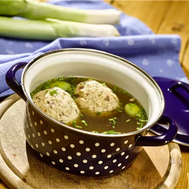 A bowl of broth with two dumplings in it. Fresh spring onions are visible in the background.