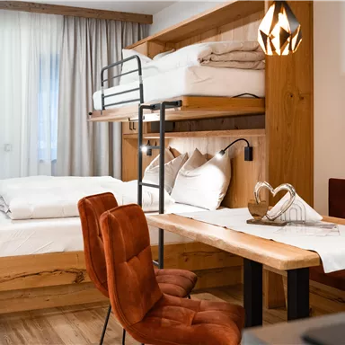 Ein gemütliches Zimmer mit einem Doppelbett und einem Hochbett. Der Raum ist modern eingerichtet und bietet einen Essbereich mit einem Tisch und Stühlen.
