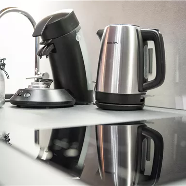 Eine moderne Küchenecke mit einem Wasserkocher und einer Kaffeemaschine. Der glänzende Kochfeldreflex zeigt die Geräte elegant.