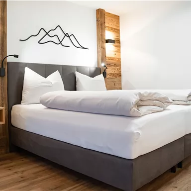 Ein modernes Schlafzimmer mit einem Doppelbett und Holzdekor. An der Wand sind stilisierte Bergmotive und Lichter angebracht.