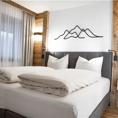 Ein modernes Schlafzimmer mit einem großen Bett und zwei kissen. An der Wand hängt eine stilisierte Berggrafik, und die Einrichtung ist aus Holz.