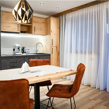 Eine moderne Küche mit einem Holz-Esstisch und stilvollen Stühlen. Große Fenster lassen viel Licht hereinfällen.