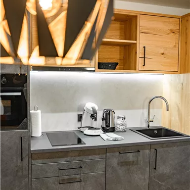 Eine moderne Küche mit grauen Schränken und Holzregalen. Die Ausstattung umfasst eine Kaffeemaschine, einen Wasserkocher und eine Spüle.
