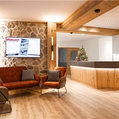 Ein eleganter Empfangsbereich mit modernen Möbeln und warmem Holzdesign. Im Hintergrund fehlt ein Weihnachtsbaum, der eine einladende Atmosphäre schafft.