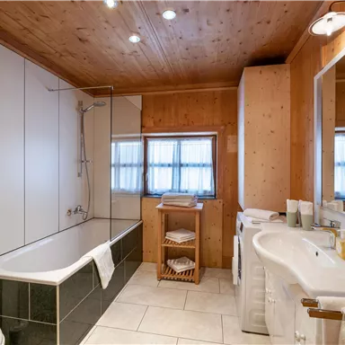 A modern bathroom with a bathtub and a sink. The walls are light with wood paneling and large windows for natural light.