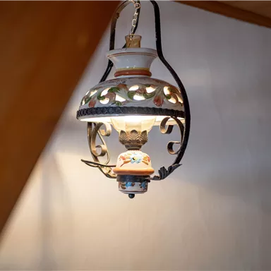 A decorative table lamp hangs from the ceiling. It has an ornate design with colorful embellishments and emits warm light.