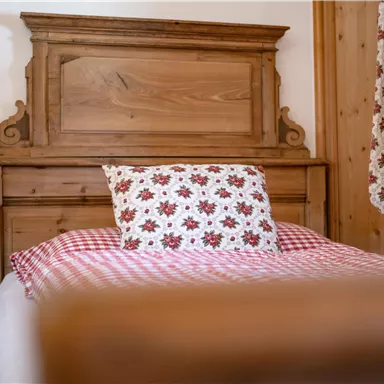 A cozy bedroom with a wooden headboard and a checked bed sheet. The pillow has a blooming pattern and a warm, inviting atmosphere.