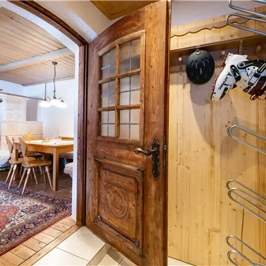 An inviting entrance area with a beautiful wooden door and a coat rack. In the background, a dining area with a table and chairs can be seen.