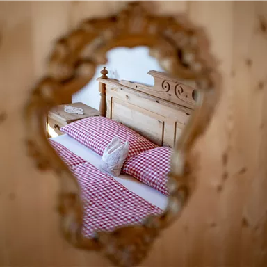 A cozy bedroom with a wooden bed and checkered pillows. The view is framed by an elegant mirror.