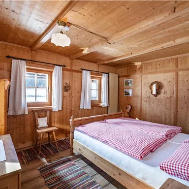 A cozy bedroom with wood paneling and a large bed. The windows let in a lot of light, and the decor is simple and welcoming.