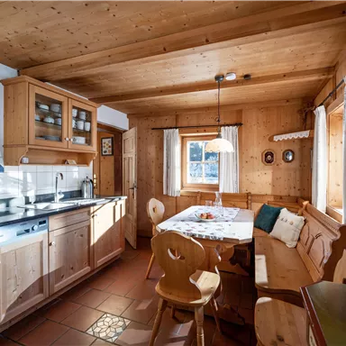 A cozy kitchen with wooden surfaces and a dining area. The light falls through a window, creating an inviting atmosphere.