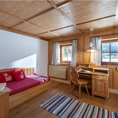 A cozy wooden bedroom with a single bed, a desk, and a chair.  

Large windows provide plenty of daylight and a view outside.