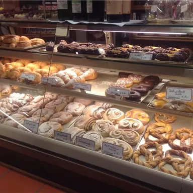 Eine ansprechende Auswahl an Gebäck in einer Bäckerei. Verschiedene Brötchen, Krapfen und süße Teilchen sind auf einem Regal ausgestellt.