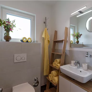 Ein modernes Badezimmer mit hellem Design und einer eleganten Einrichtung. Gelbe Handtücher und Pflanzen sorgen für einen freundlichen Akzent.