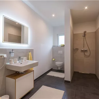 Ein modernes Badezimmer mit einer Dusche und einem Waschbecken. Helle Wände und gelbe Handtücher sorgen für eine freundliche Atmosphäre.