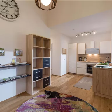 Eine moderne Küche mit Holzregalen und einem runden Teppich liegt im Fokus des Bildes. Es gibt helle Wände und eine gemütliche Atmosphäre.