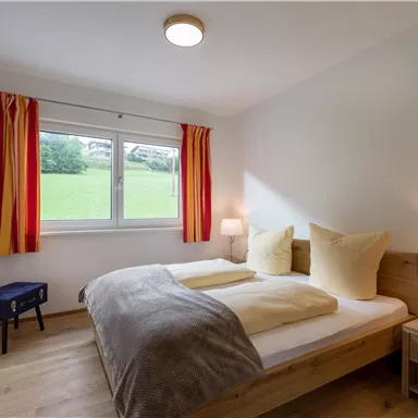 Ein gemütliches Schlafzimmer mit einem Doppelbett und hellen Kissen. Das Zimmer hat ein großes Fenster mit Blick auf eine grüne Wiese.