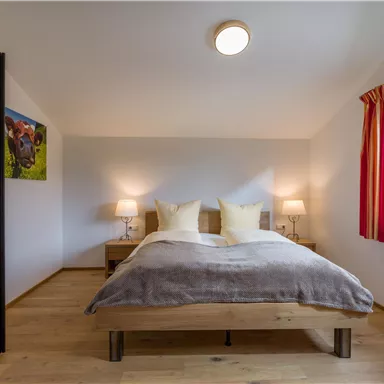 Ein gemütliches Schlafzimmer mit einem Doppelbett und zwei Nachttischen. Große Fenster sorgen für viel Tageslicht und eine angenehme Atmosphäre.