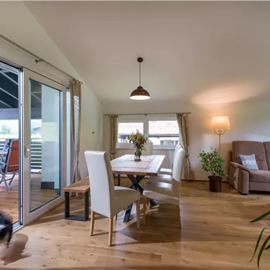 Ein helles und offenes Wohnzimmer mit einem Essbereich und einer bequemen Couch. Große Fenster lassen viel Tageslicht herein und schaffen eine einladende Atmosphäre.
