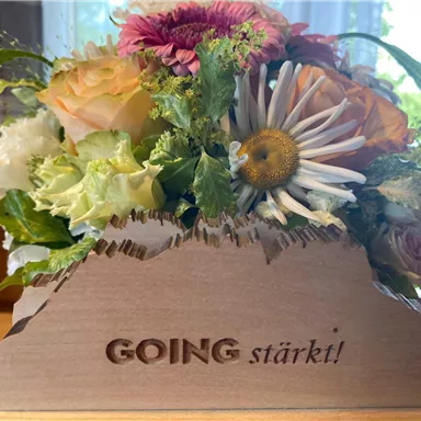 Ein schöner Blumenstrauß mit bunten Blumen und grünen Blättern in einer Holzkiste. Auf der Kiste steht die Aufschrift „GOING stärkt!“.