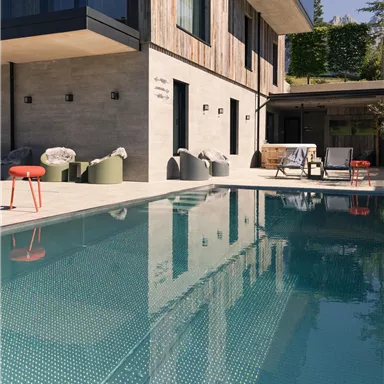 A modern house with a pool and a beautiful terrace. The clear water surface reflects the architecture of the building.