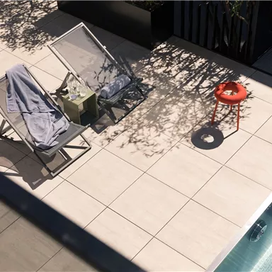 A sunny terrace with two loungers and a red stool. Next to the pool, there is a towel on the loungers.