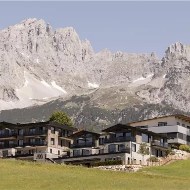 A modern building in a hilly landscape, surrounded by majestic mountains. The clear air and the impressive nature create a serene atmosphere.