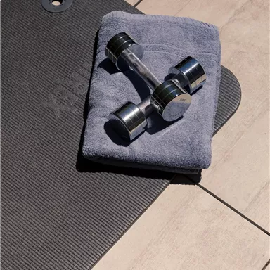 A training area with a yoga mat and a dumbbell on a towel. The floor is made of light tiles.