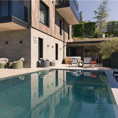 A modern house with a swimming pool and stylish lounge furniture. The outdoor area is bright and inviting, surrounded by green vegetation.