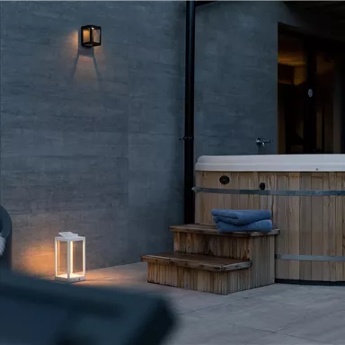 A cozy outdoor area with a wooden hot tub and a small staircase. Soft lighting creates a relaxed atmosphere.