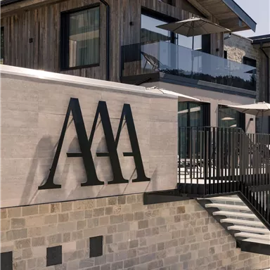 A modern building with wooden elements and large windows. The inscription "AAA" is clearly visible on the wall.