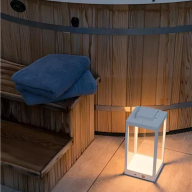 A relaxing hot tub with wooden cladding. Next to the hot tub lies a towel and a glowing lantern.