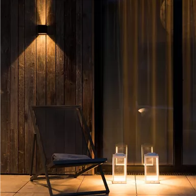 A cozy balcony with a chair and two glowing lanterns. The atmosphere is warm and inviting at dusk.