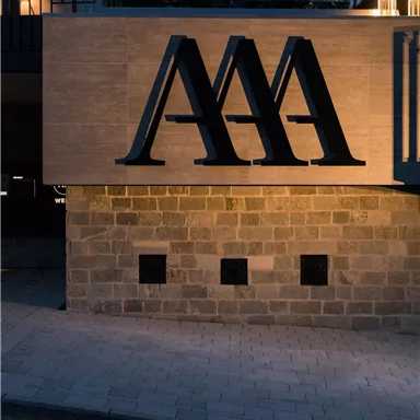 A modern sign with the logo "AAA" in stylish black. It is illuminated at night and is located on a building.