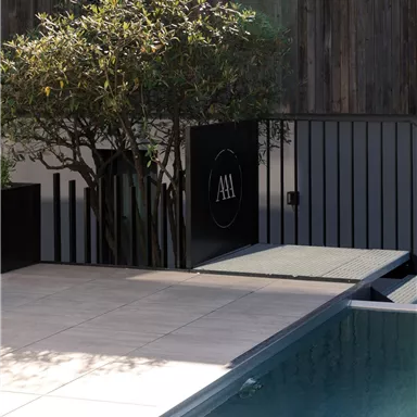 A modern pool area with a small tree and stylish stone tiles. The atmosphere is quiet and inviting.