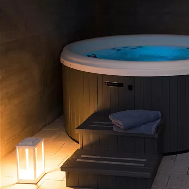 A relaxing hot tub in a dark room, surrounded by soft lighting. A small step and a towel are ready.