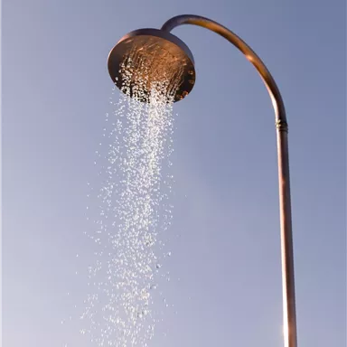 A modern shower head with water splashing into the air. The sky is clear and blue.