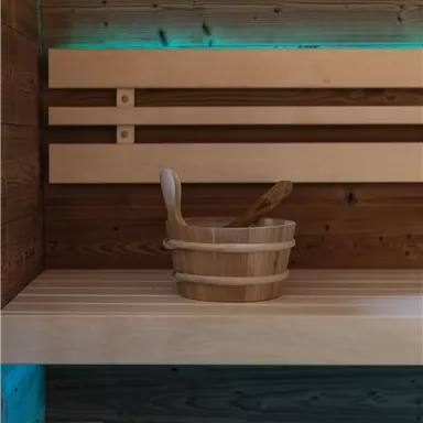 A wooden club and a scoop are resting on a sauna-appropriate bench. The soft lighting creates a relaxed atmosphere.